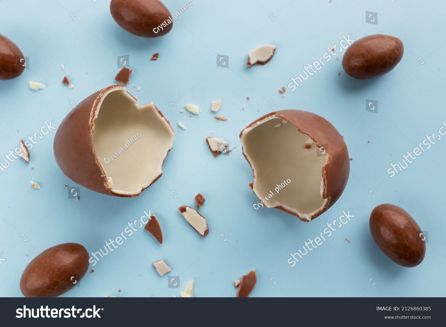 stock photo two halves of a broken chocolate egg for children a chocolate egg with small eggs around on a blue 2126860385